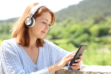 Woman wearing wireless headphones listening to music using phone in a balconyの写真素材
