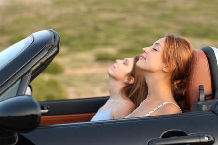 Side view portrait of two women resting breathing fresh air in a convertible carの写真素材
