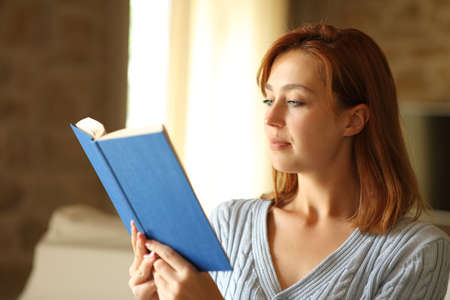 Concentrated woman reading a paper book in the living room at homeの写真素材