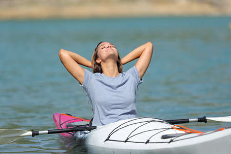 Happy woman in a kayak relaxing with arms on head in a lakeの写真素材