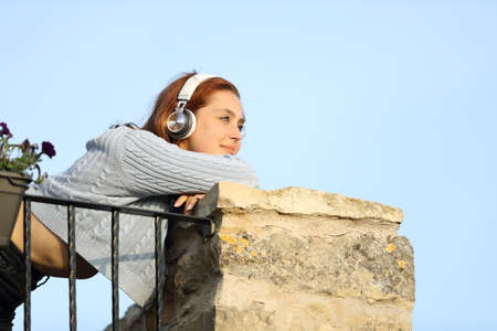 Happy woman contemplating from balcony listening to music with headphonesの写真素材