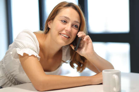 Happy woman talking on smart phone looking away sitting at homeの写真素材