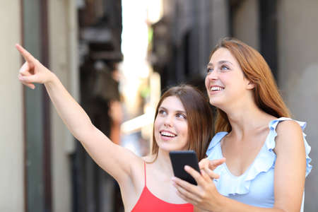 Two happy women using smart phone and pointing up in the streetの写真素材