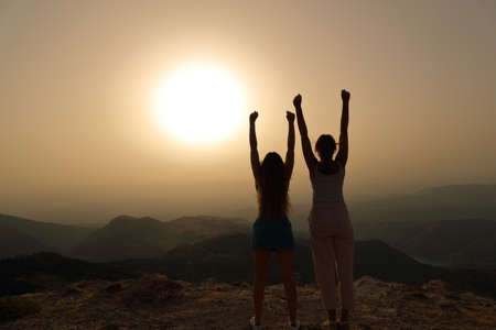 Back view portrait of a women silhouette raising arms celebrating at sunset