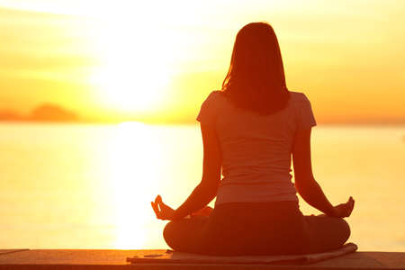Back view full body of woman silhouette doing yoga at sunset on the beachの写真素材