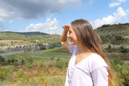 Happy woman looking away protecting from sun with her hand in the mountainの写真素材