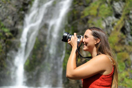 Side view portrait of a happy woman taking photos with mirrorless camera in natureの写真素材