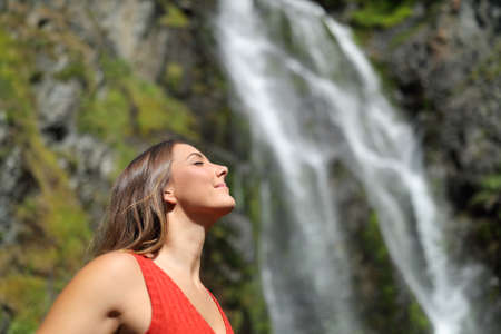 Side view portrait of a relaxed woman breathing fresh air in a waterfallの写真素材