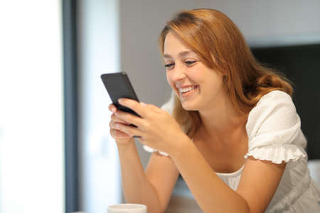 Happy woman using smart phone checking content smiling at homeの写真素材
