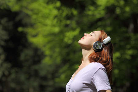 Profile of a woman relaxing meditating listening audio with wireless headphones in a sunny park