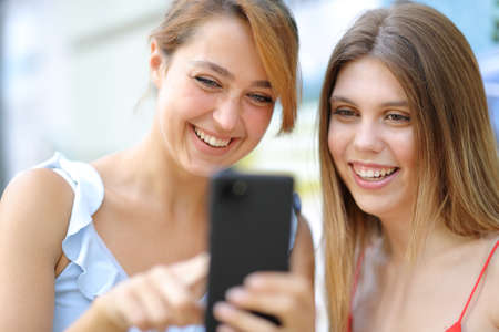 Two happy friends using smart phone and laughing in the streetの写真素材