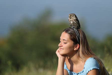 Relaxed woman enjoying nature sitting with an owl perched on headの写真素材
