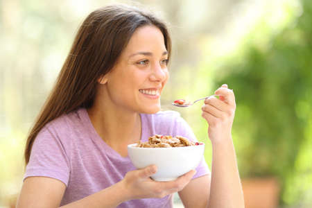 Happy woman eating cereal looking away in terraceの写真素材