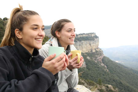 Two happy trekkers drinking coffee and contemplating in a cliffの写真素材
