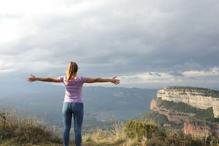 Back view of a woman outstretching arms in the top of a cliffの写真素材