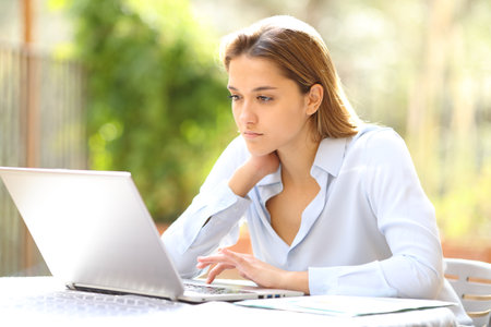 Serious businesswoman working online with laptop in terraceの写真素材