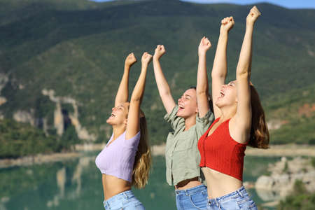 Three happy friends celebrating vacation raising arms in a mountain lakeの写真素材
