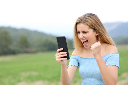 Excited teen checking online content on smart phone in a fieldの写真素材