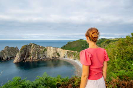 Back view portrait of a woman contemplating a beautiful coast on summer vacationの写真素材