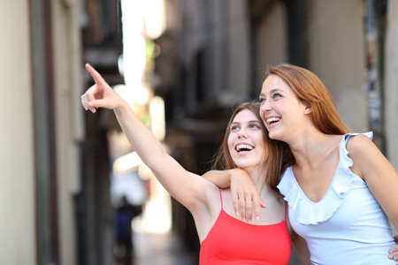 Two happy friends laughing together pointing up in the streetの写真素材
