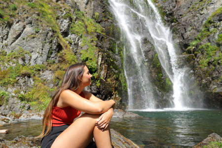 Happy woman sitting alone contemplating a beautiful waterfallの写真素材