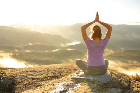 Back view portrait of a woman doing yoga pose in the mountain at sunriseの写真素材