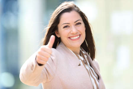 Happy businesswoman standing in the street with thumbs up looking at cameraの写真素材