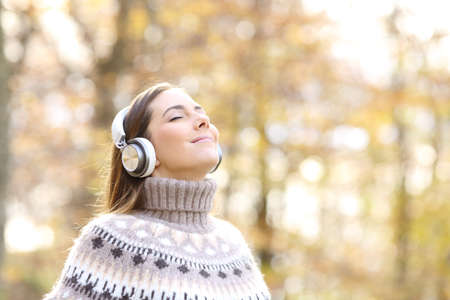 Relaxed woman listening to music and breathing fresh air in autumn in a forest or parkの写真素材
