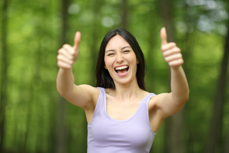 Front view portrait of a happy asian woman gesturing both thumbs up in a parkの写真素材