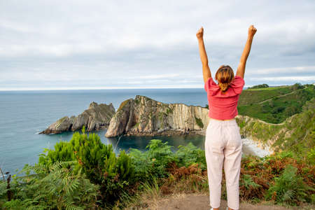Back view portrait of an excited tourist raising arms celebrating summer vacation in a beautiful coastの写真素材