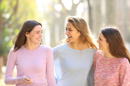 Three happy friends talking and laughing walking in the streetの写真素材