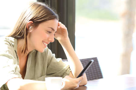 Happy woman reding message on smart phone in a coffee shopの写真素材