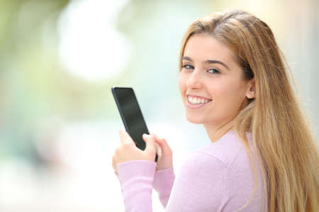 Happy woman using smart phone and looking at camera standing in a parkの写真素材