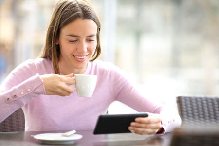 Happy woman watching media on smart phone drinking in a barの写真素材