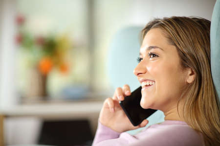 Happy woman is talking on mobile phone sitting on a couch at homeの写真素材