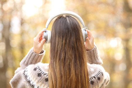 Back view portrait of a woman in winter putting headphones in a parkの写真素材