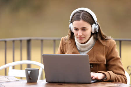Woman wearing headphones watching media content on laptop in a terrace in winterの写真素材