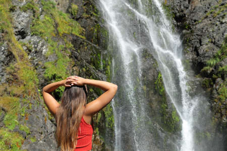 Back view of a woman contemplating waterfall in the mountainの写真素材