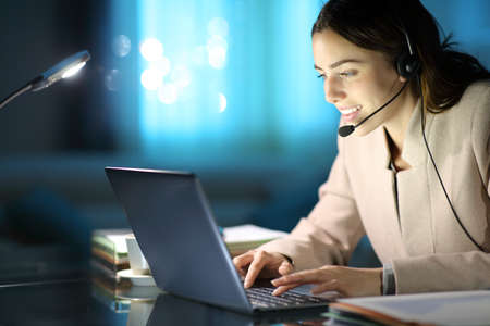 Happy tele marketer working with headset and laptop in the night at homeの写真素材