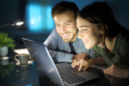 Happy couple watching content on laptop in the night at homeの写真素材