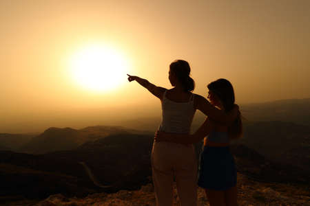 Back light silhouette of two women pointing sun at sunsetの写真素材