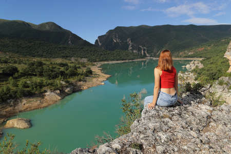 Woman contemplating views of a lake sitting in a cliff on summer vacationの写真素材