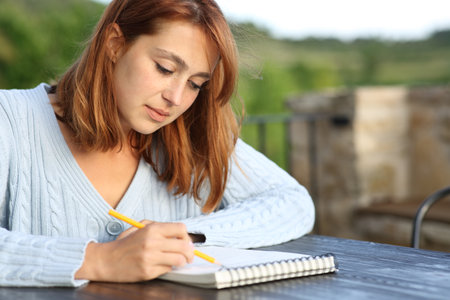 Concentrated woman drawing on paper notebook in a terrace at homeの写真素材