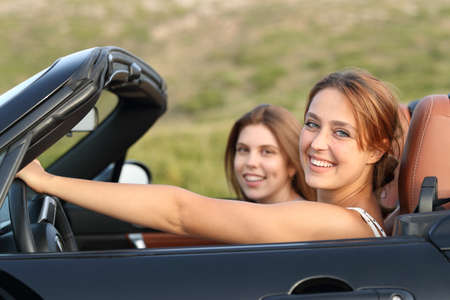 Two happy friends looking at you in a convertible car in the mountainの写真素材