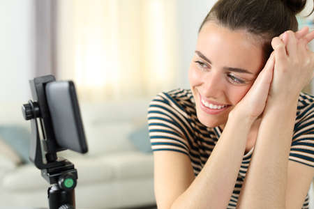 Happy woman watching videos on smartphone sitting at home