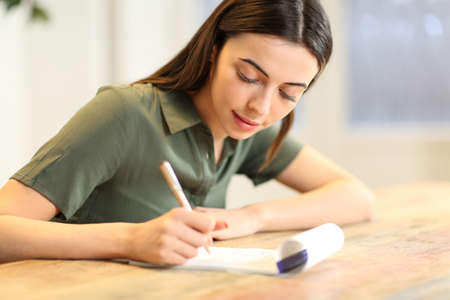 Happy woman taking notes on paper notebook on table at home