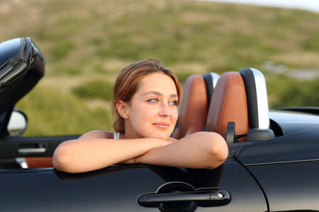 Satisfied owner looking away in a cabriolet car in the mountainの写真素材