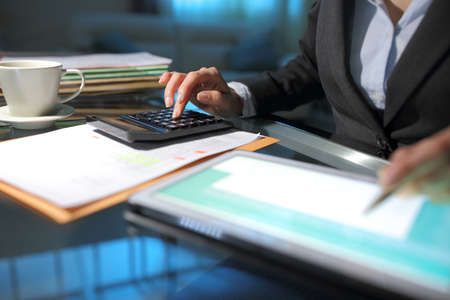Businesswoman hand accounting using calculator and tablet on a desk in the night at officeの写真素材