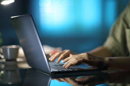 Close up of a woman hands typing on laptop in the night at home