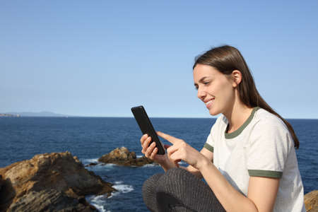 Happy woman checking smart phone content on the coastの写真素材